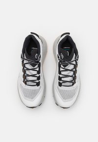 Hvite atletiske sko med mesh-overdel og grå accenter. Har svarte lisser, en polstret krage og en strukturert gummisåle med oransje detaljer.