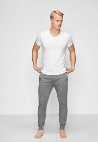 Hvid V-hals t-shirt og grå bomulds joggebukser. T-shirten har korte ærmer, og joggerne har elastiske manchetter og en blød tekstur.