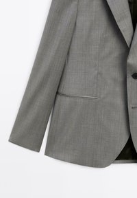 Grauer maßgeschneiderter Blazer aus glattem, strukturiertem Stoff. Verfügt über einen Knopfverschluss und zwei Vorder Taschen. Scharfe Revers und lange Ärmel.
