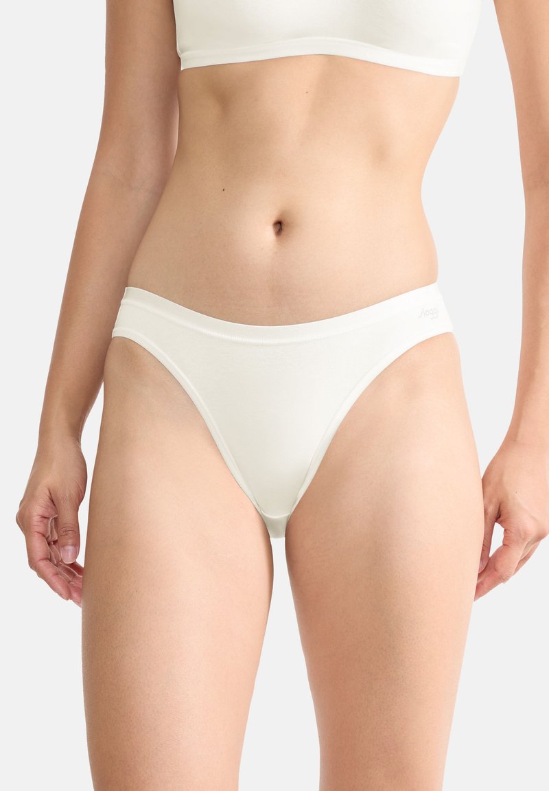 Femme portant une culotte string blanche sans coutures et un soutien-gorge assorti, vue du ventre jusqu'en haut des cuisses sur un fond neutre.