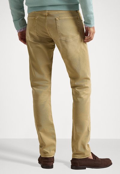 Μπεζ τζιν παντελόνι ίσιας γραμμής φτιαγμένο από βαμβάκι, με πίσω τσέπες και ραφές, σε συνδυασμό με σκούρες καφέ σουέντ μοκασίνια.