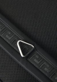 Fekete, texturált anyag, hálós mintával és háromszög alakú ezüst fém D-gyűrűvel. Mintás fekete pánttal rendelkezik a rögzítéshez.