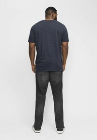 Mørkeblå t-shirt med korte ærmer og rund hals, parret med mørke denimjeans. Outfittet har en afslappet pasform og en glat tekstur.