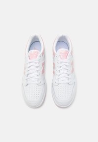 Paire de baskets blanches New Balance avec des accents rose clair, lacées et vues de dessus sur un fond blanc uni.