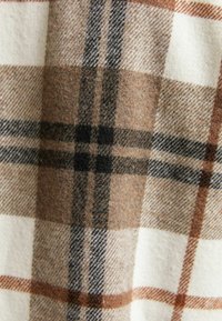 Brązowo-kremowa tkanina w kratę z czarnymi akcentami; wełnista tekstura z różnorodnymi wzorami dużych i małych kratek. Miły w dotyku i ciepły wygląd.