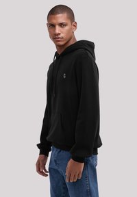 Black hoodie made of cotton with a front pocket and adjustable drawstring hood. Features a small logo on the chest. Classic fit.