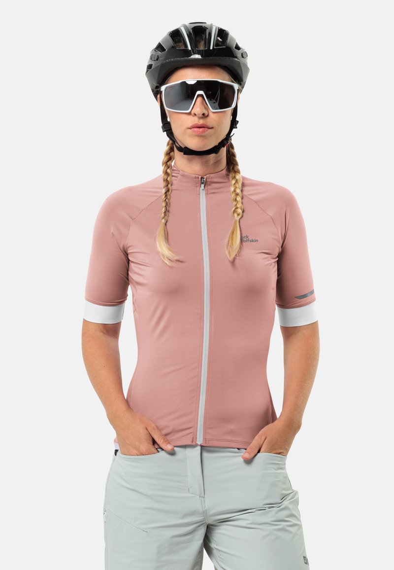 Maillot de cyclisme rose à manches courtes avec une fermeture éclair intégrale, des accents blancs et un logo. Le modèle porte un casque noir et des lunettes de soleil. Short gris clair.