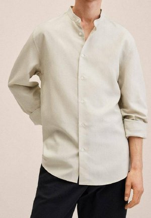 Chemise collerette beige clair, boutonnée, avec des manches longues retroussées. Texture de tissu douce, coupe droite et léger éclat.