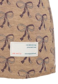 Brązowa tkanina z powtarzającym się wzorem niebieskich i ciemnofioletowych kokardek. Zawiera białą etykietę z tekstem w kolorze niebieskim i czerwonym.