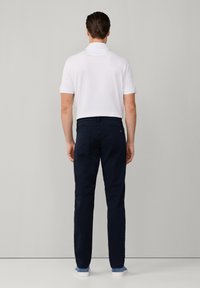 Camisa polo blanca de manga corta combinada con pantalones azul marino y zapatillas blancas. Los pantalones cuentan con bolsillos traseros y un diseño ajustado.