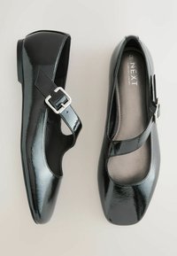 Black patent Mary Jane shoes with a square toe, cut-out design, and a silver buckle strap. Soft insole and flat heel.