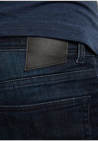 Tmavě modré džíny s černou koženou nášivkou značky "CHASIN'", které mají texturovaný denim a jemné šití.