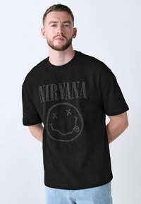 Black cotton t-shirt featuring a rhinestone Nirvana graphic on the front, short sleeves, and a crew neckline. Classic slim fit design.