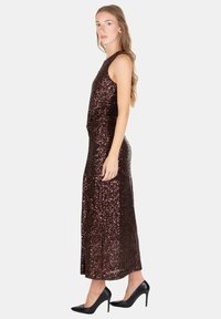 Abito da sera marrone con paillettes, dal taglio aderente, senza maniche e con uno spacco laterale, abbinato a scarpe con tacco alto nere.