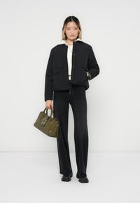 Veste matelassée noire avec fermeture à boutons et deux poches avant, portée sur un pull crème. Associée à un pantalon noir évasé et un sac à main olive.