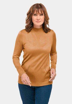 Brauner Pullover mit langen Ärmeln und hohem Kragen, der strukturierte Akzente in der Taille aufweist und eine glatte Oberfläche hat, kombiniert mit blauen Jeans.