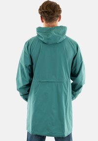 Veste imperméable teal avec capuche, dotée d'une coupe décontractée, de manches longues et d'une poche arrière. Texture lisse, adaptée à un usage en extérieur.