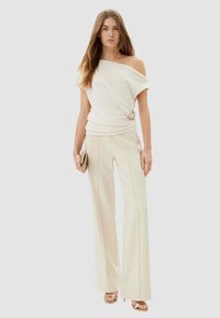 Top crema scivolato sulle spalle, drappeggiato in vita, abbinato a pantaloni crema a gamba larga con sottili righe a spina di pesce. Dettaglio dorato in vita.