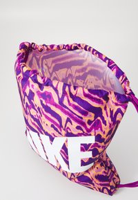 Violetinė ir rožinė raišteliu uždengiama kuprinė su sukimosi raštu, iškilmingai turinti didelį baltą "NIKE" logotipą priekyje ir lygią vidinę tekstūrą.