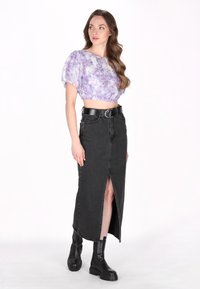 Fliederfarbene Blümchen-Crop-Top mit Puffärmeln, kombiniert mit einem schwarzen Denim-Maxirock mit einem Schlitz vorne und einem breiten schwarzen Gürtel. Schwarze Stiefeletten.