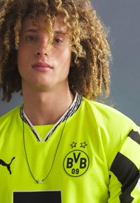 Fényes sárga sportmez fekete csíkokkal, csillagokkal díszített címerrel és "BVB 09" logóval, kerek nyakkal és texturált anyaggal.