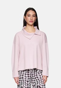 Pink cropped sweatshirt with a wide, folded collar, featuring long sleeves and a smooth texture, paired with black and white checkered pants.