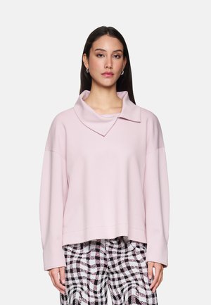 Rosa, kürzer geschnittenes Sweatshirt mit einem breiten, umgeschlagenen Kragen, langen Ärmeln und einer glatten Textur, kombiniert mit schwarz-weiß karierten Hosen.