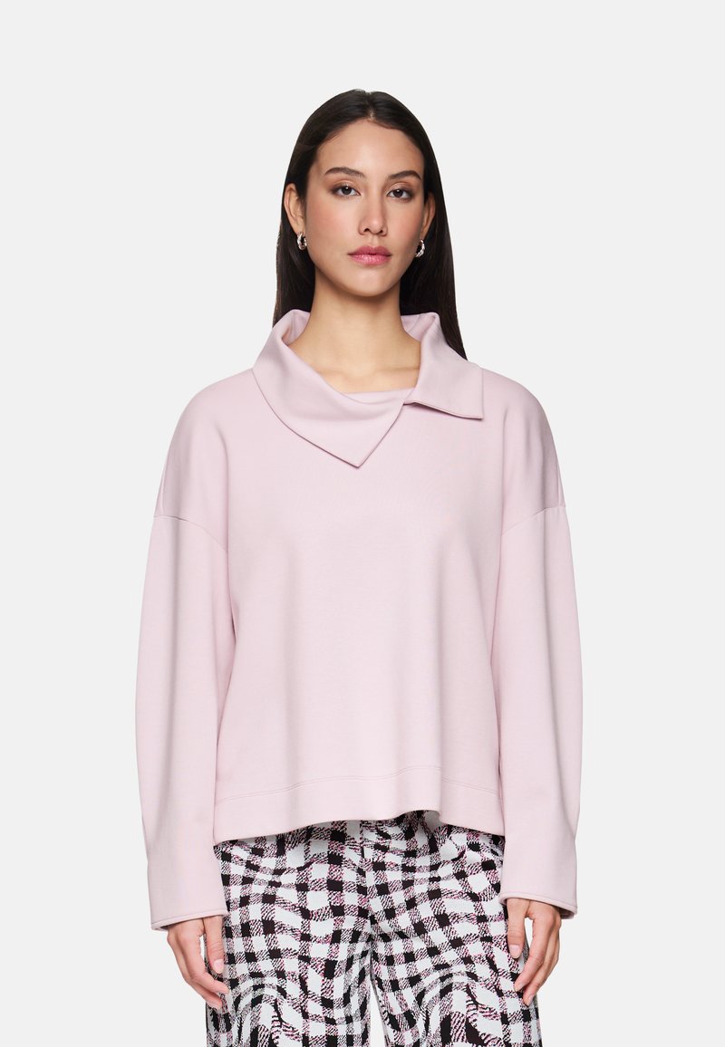 Pink cropped sweatshirt with a wide, folded collar, featuring long sleeves and a smooth texture, paired with black and white checkered pants.