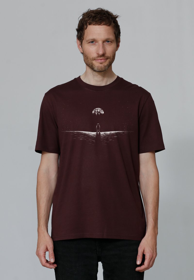 Bordeaux T-shirt, ronde hals, korte mouwen. Heeft een witte afbeelding van een figuur en een boom op een golvend ontwerp. Zachte katoenkwaliteit.