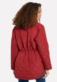 Giacca trapuntata rossa con vita elasticizzata, maniche lunghe e texture a motivo arrotondato. La vista posteriore mostra una vestibilità relaxed e un tessuto morbido.
