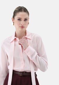 Light pink button-up shirt with a large collar, long sleeves, and a matching neck tie, paired with dark brown belted trousers. Smooth texture.