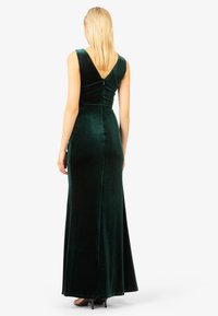 Groene fluwelen lange jurk met een aansluitende corsage en V-vormige achterkant. Vloerlange silhouet met een gladde textuur en subtiele glans.