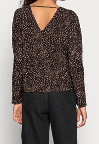 Top nero con scollatura a V e maniche lunghe, con un motivo a stampa leopardo in tonalità di marrone. Mostra dettagli sul retro con una cintura.