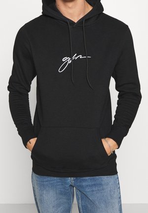 Haut à capuche noir avec cordon de serrage, poche avant et texte brodé blanc. Manches longues et finition en tissu doux et lisse. Coupe décontractée.