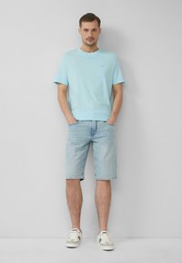 Jasnoniebieska koszulka z krótkim rękawem z miękkiego materiału, połączona z jasnoniebieskimi szortami dżinsowymi. Buty mają neutralną kolorystykę z akcentami.