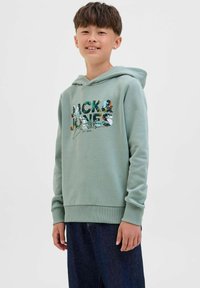Felpa verde con tasca a marsupio e polsini a coste, con una grafica colorata "Jack & Jones" sul davanti, abbinata a jeans scuri.