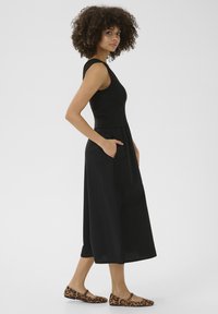 Svart ärmlös klänning med en figurnära bodice och vid kjol, försedd med sidofickor. Kombinerad med lägenheter i leopardmönster.