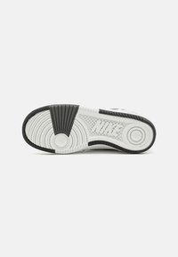 White sole with black rubber accents and textured tread patterns. Features circular and horizontal designs, branded with "NIKE" on the side.