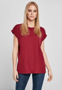 Rdeča majica s kratkimi rokavi in sproščenim krojem, izdelana iz mehke bombažne tkanine. Ima preprost okrogel izrez in zavihane rokave.