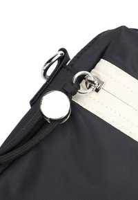 Black nylon bag featuring a cream-colored stripe, silver hardware, a zipper with a cord pull, and a circular metal accent.