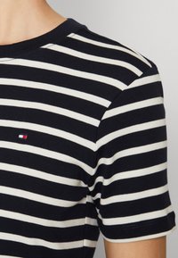Meriini sininen ja valkoinen raidallinen T-paita pyöreällä kauluksella ja lyhyillä hihoilla. Rinnassa pieni logo. Pehmeää puuvillakangasta.