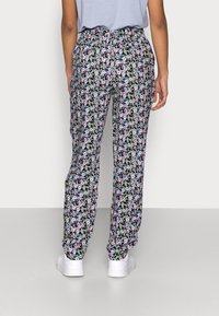 Blommiga pyjamasbyxor med svart bakgrund, med ett färgglatt mönster av små blommor. Elastisk midja; lösa ben som smalnar av nedåt. Vita skor.