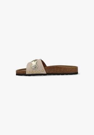 Beige suède slippers met kurken zool, zwarte loopzool, gouden metalen vlinderversiering en vijf gouden studs op het bandje.
