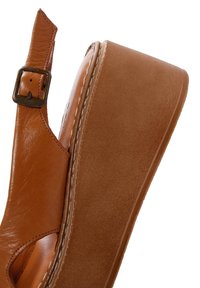 Sandale plateforme en cuir marron avec une large base, un design ouvert, une sangle de cheville ajustable et un détail de couture proéminent le long du bord.