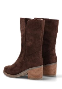 Botas de tobillo de ante marrón con punta redonda, costuras mínimas y un tacón apilado y texturizado. Sin hardware visible ni adornos.