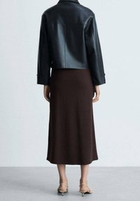 Schwarze Leder-Cropped-Jacke über einem braunen, figurbetonten Midikleid, das eine glatte Textur und ein einfaches, elegantes Design aufweist. Klare Silhouette und keine Muster.