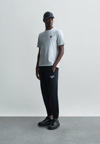 Tricou gri cu mâneci scurte și un mic emblemă cu tigru, asortat cu pantaloni negri pe care este scris "modern, viitor". Tenis negri completează ținuta.