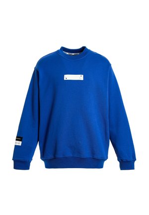 Sudadera azul hecha de tejido suave, con cuello redondo, mangas largas, un parche rectangular blanco en el pecho y una marca en la manga.