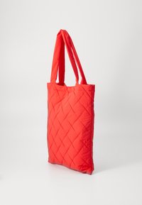 Gestepptes rotes Tote-Bag mit doppelten Stoffgriffen, die ein Rautenmuster aufweist. Leichtes Material sorgt für Flexibilität und Benutzerfreundlichkeit.