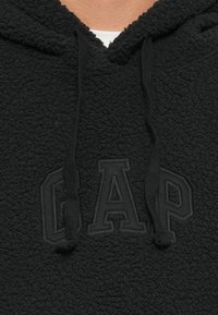 Felpa con cappuccio nera in pile caratterizzata da un tessuto testurizzato, coulisse regolabili e un logo "GAP" in rilievo sul davanti.